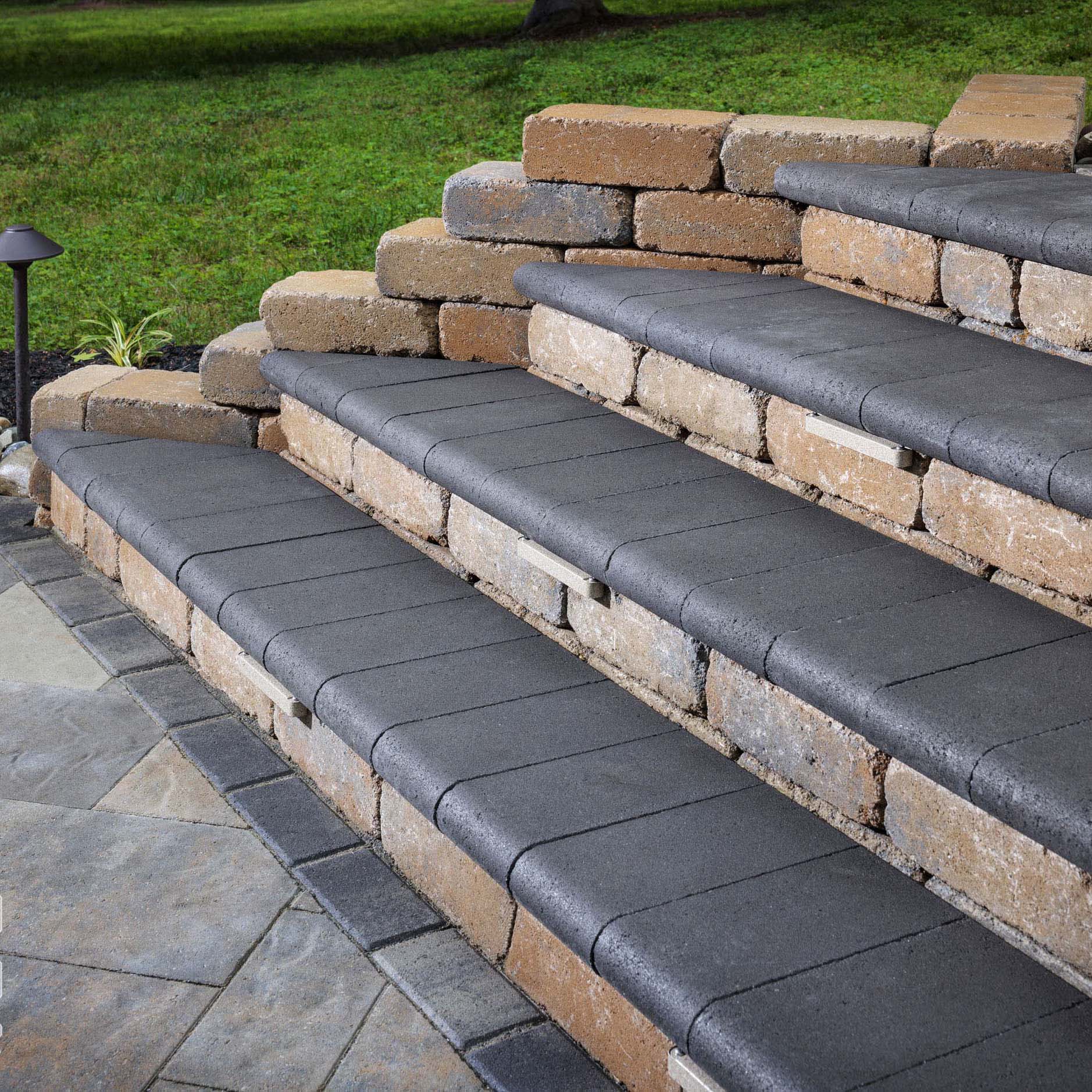 Stone steps with dark gray treads lead upward, framed by brick walls. A green lawn and pathway are visible in the background.