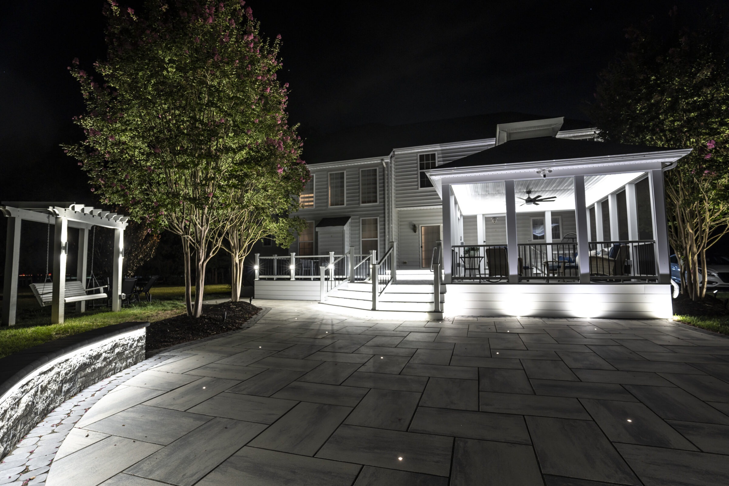 Modern house at night, featuring illuminated patio, gazebo, and swing. Surrounded by trees, creating a serene and inviting outdoor space.