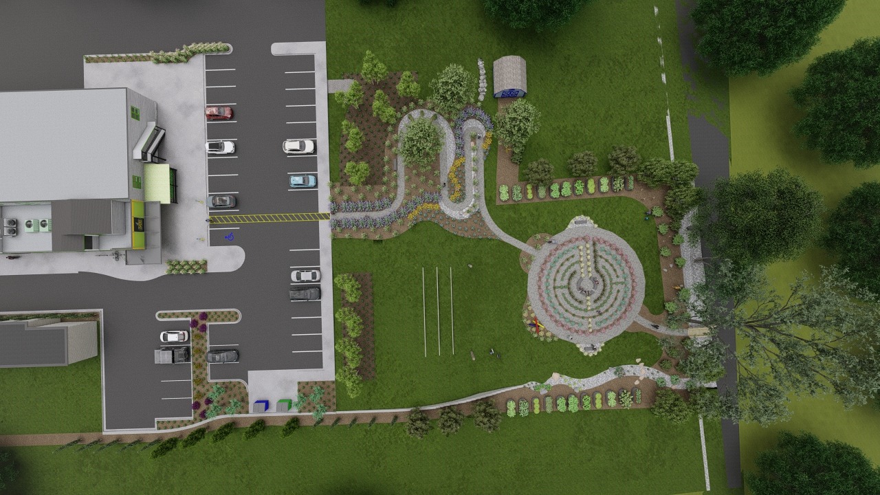 Aerial view of parking lot, adjacent building, and landscaped garden with winding pathways, circular flower arrangements, and surrounding greenery.