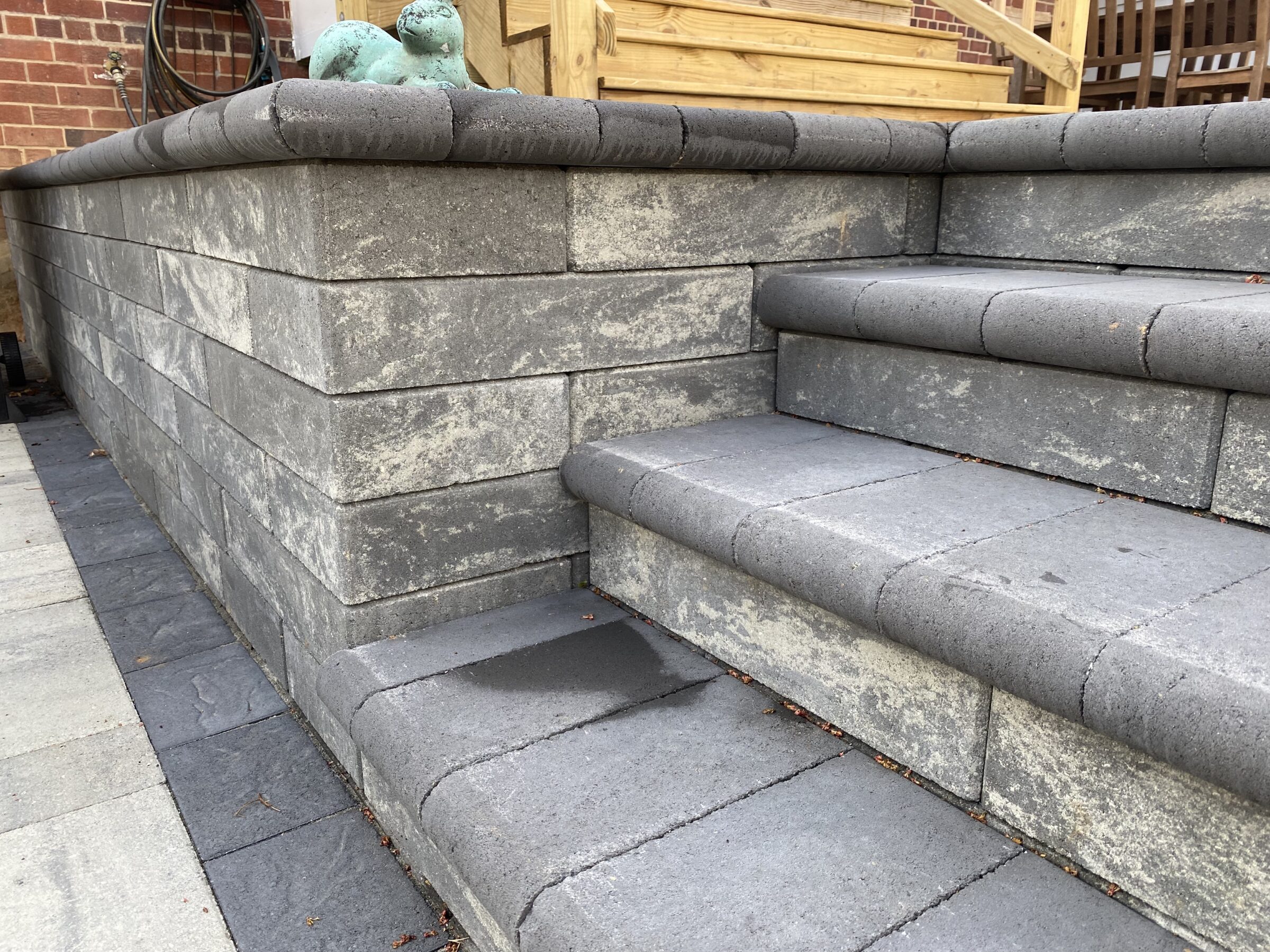 Gray stone steps and wall with a small green sculpture on top. Wooden railings and brick wall in the background.