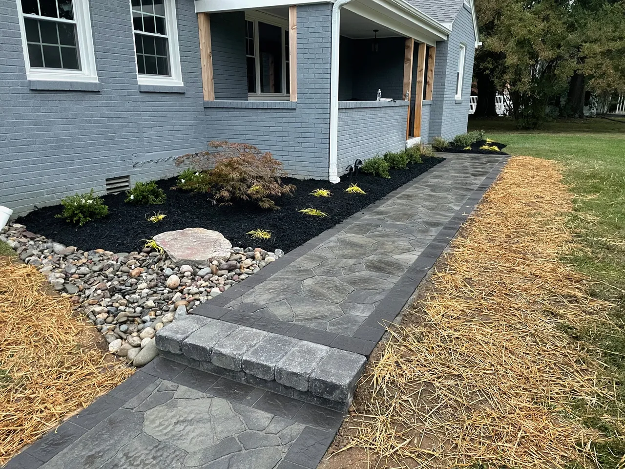 A modern house with a stone walkway, landscaped garden, and mulch-covered path leading through a neat lawn and tidy outdoor area.