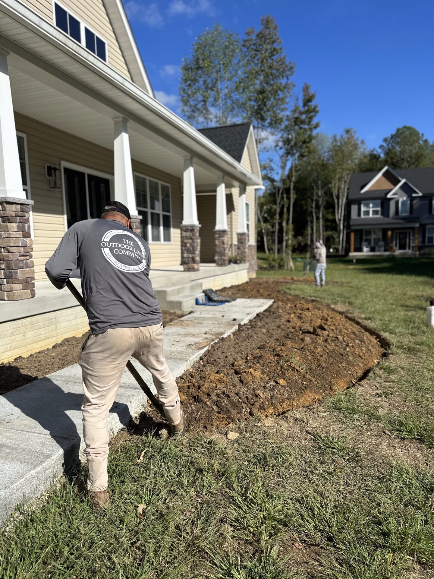 Curved stone retaining wall under construction with gravel backfill, partially enclosed patio space, and tools and materials visible on the site. The project is set in a residential backyard.