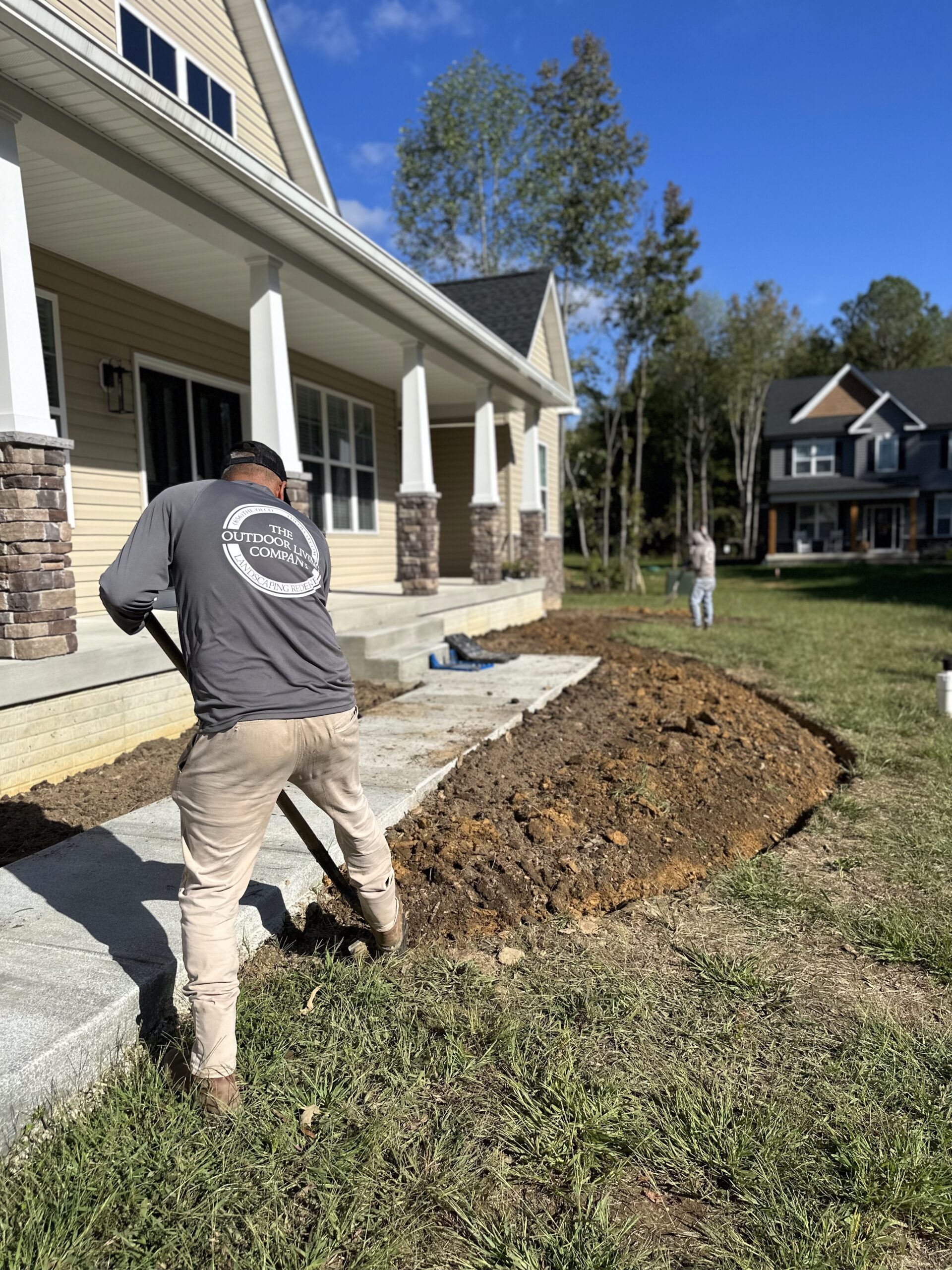 A team member helping with sustainable landscaping in Fort Washington including a curved stone retaining wall under construction with gravel backfill, partially enclosed patio space, and tools and materials visible on the site.