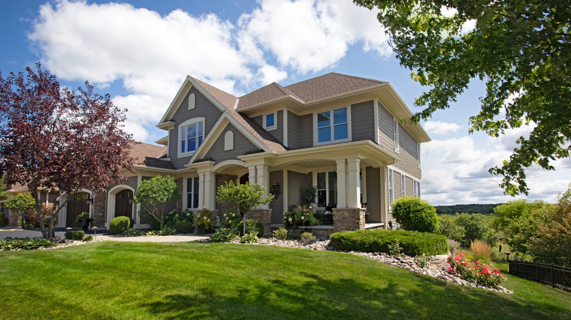 Front yard landscaping with green lawn, stone garden beds, and large two-story home.