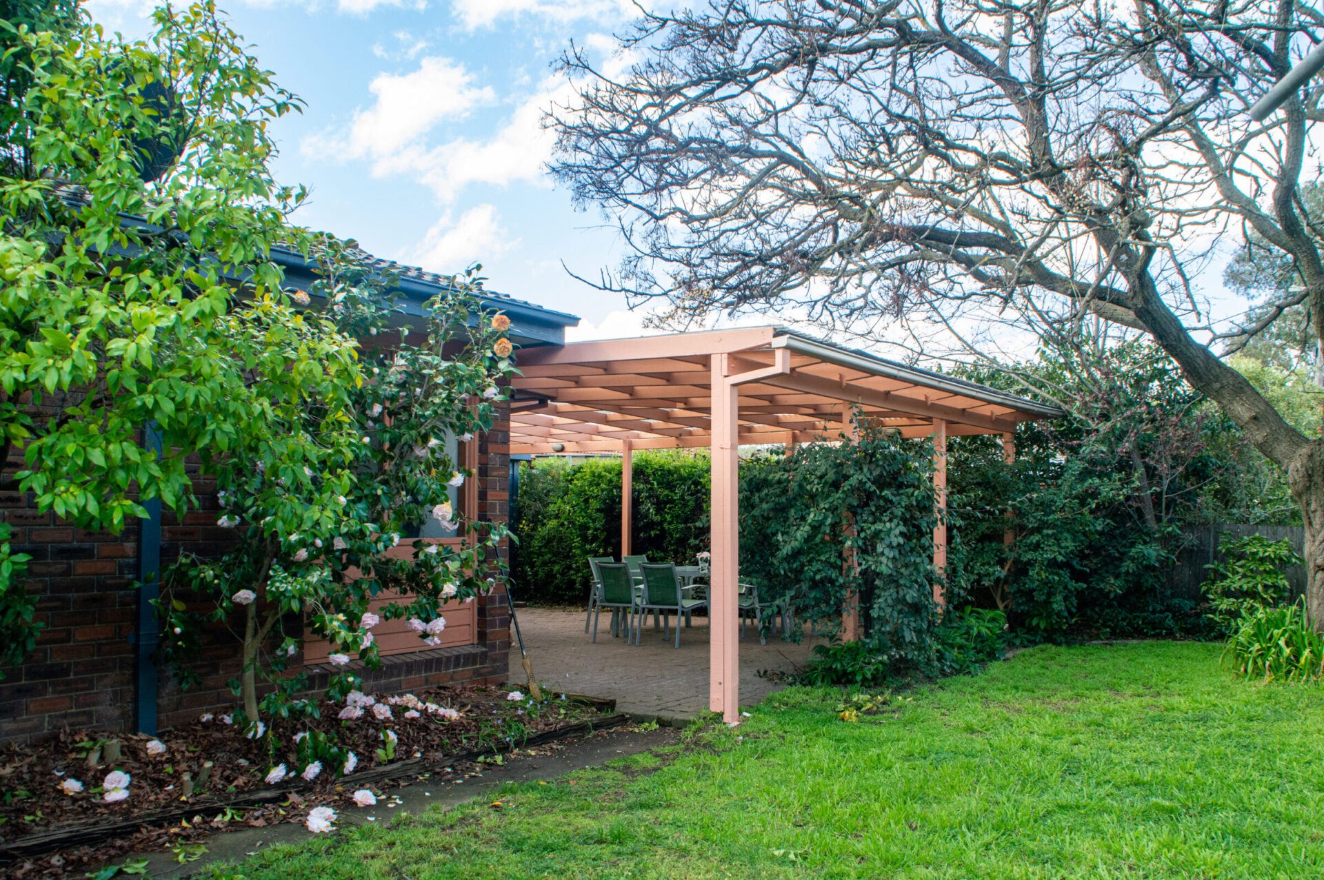 The pergola and pretty green gardens can be seen at the back of home. They are framed by a large tree and attractive bushes, as well as pretty scattered flowers.