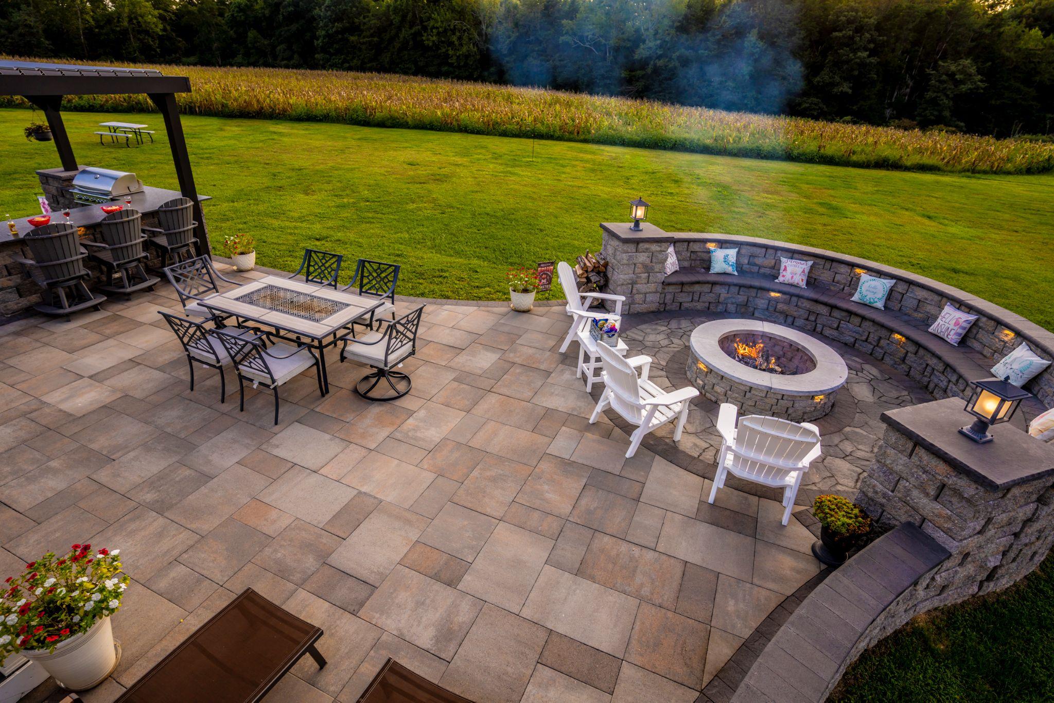 Wide paver patio with built-in curved seating around a fire pit and outdoor dining area.
