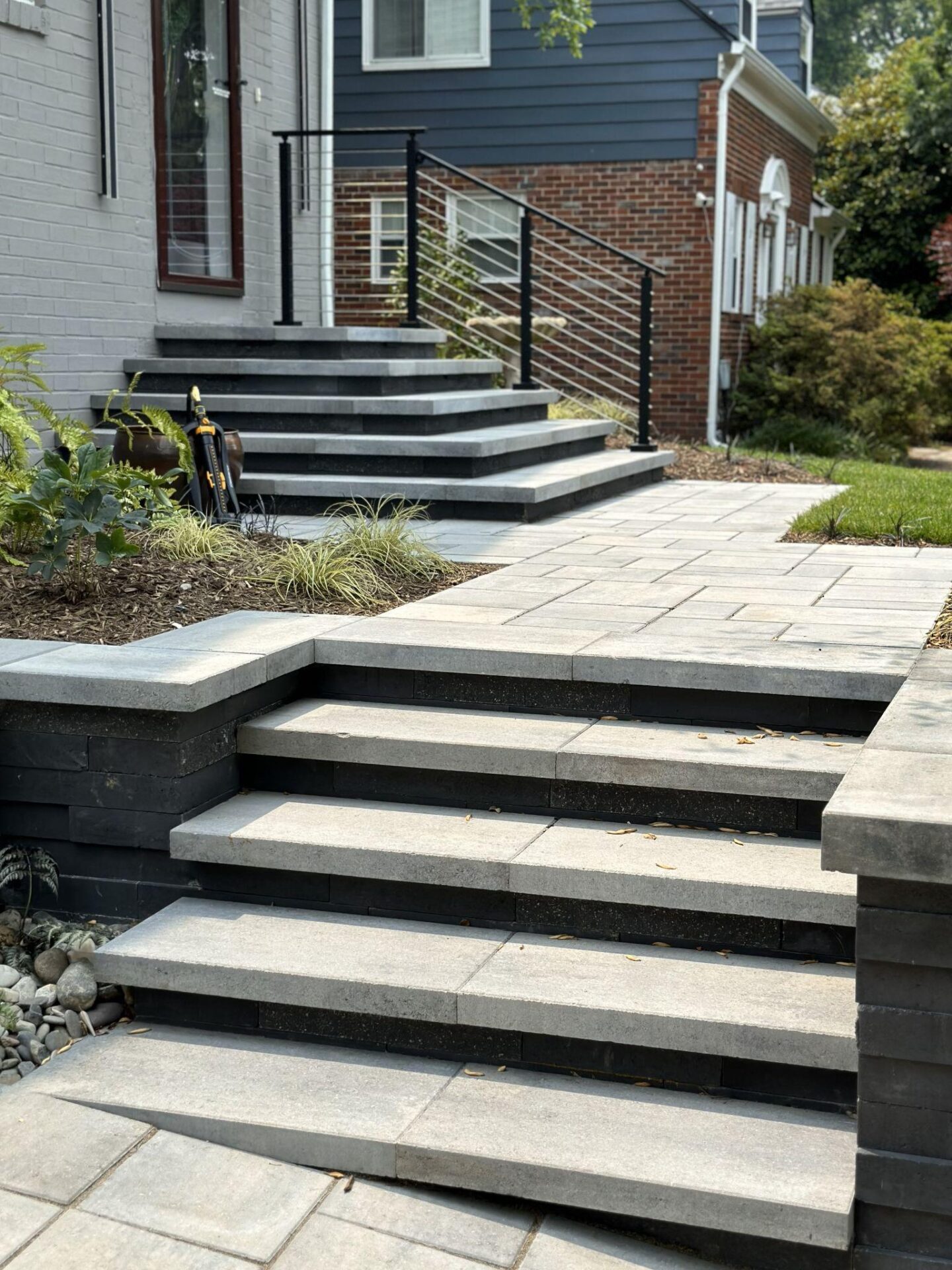 Multi-level stone steps leading to a home entrance with a modern paver walkway and railings.