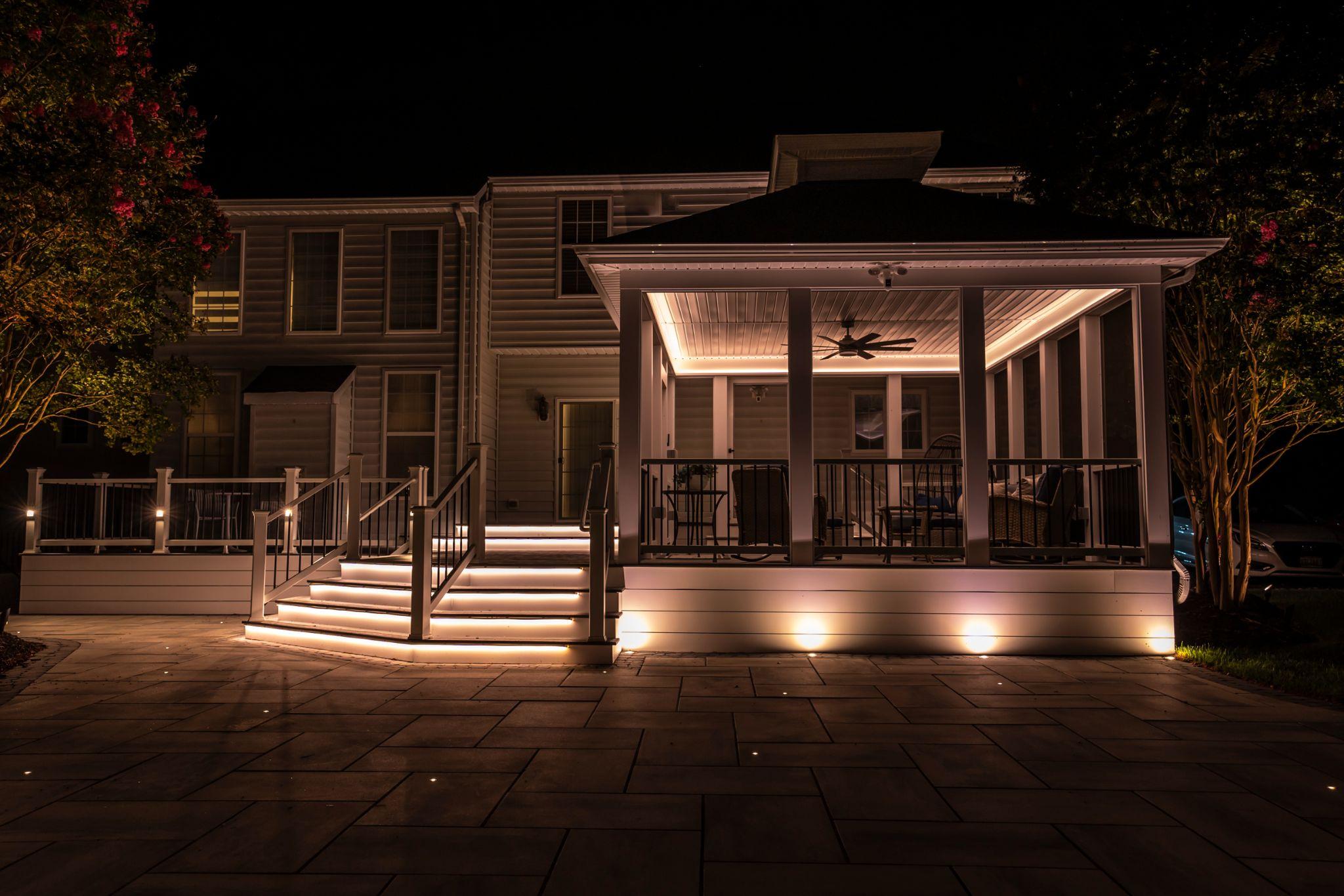 Backyard deck and patio illuminated with built-in lighting at night.