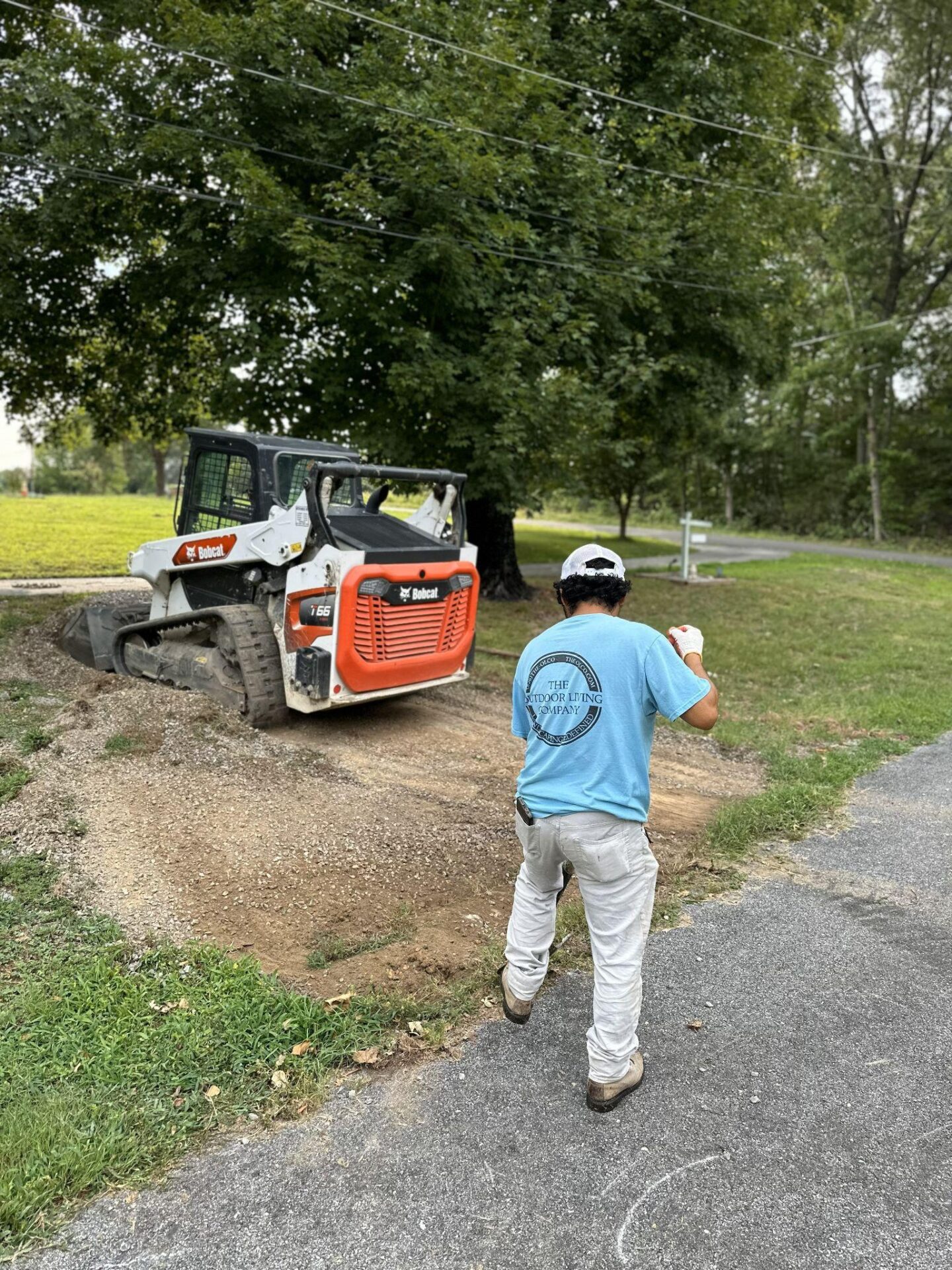 Worker standing near a skid-steer on a residential job site with trees in the background.