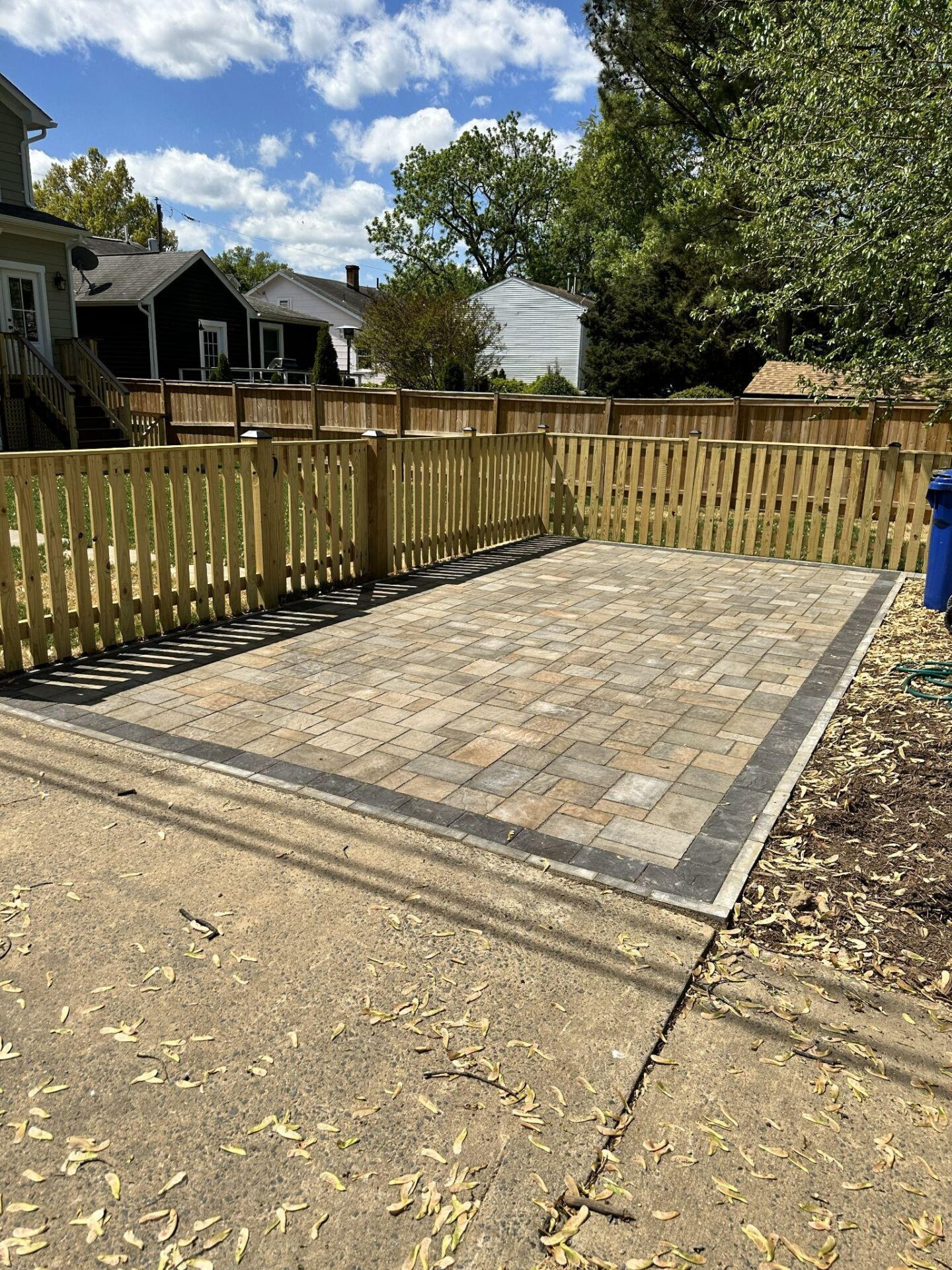 Rectangular paver parking pad bordered by wood fencing in a residential backyard.